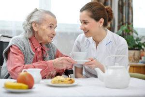 Einer älteren Frau wird von einer Pflegerin das Frühstück angereicht.