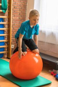 Kind bei der Kinderphysiotherapie hält kniend, ohne sich festzuhalten, Balance auf einem Gymnastikball